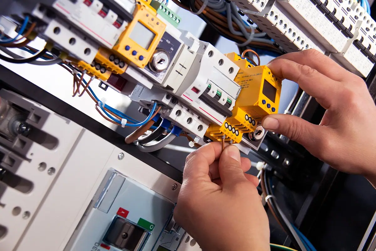 Manos de un electricista conectando un cable en un cuadro eléctrico con aparatos en carril DIN
