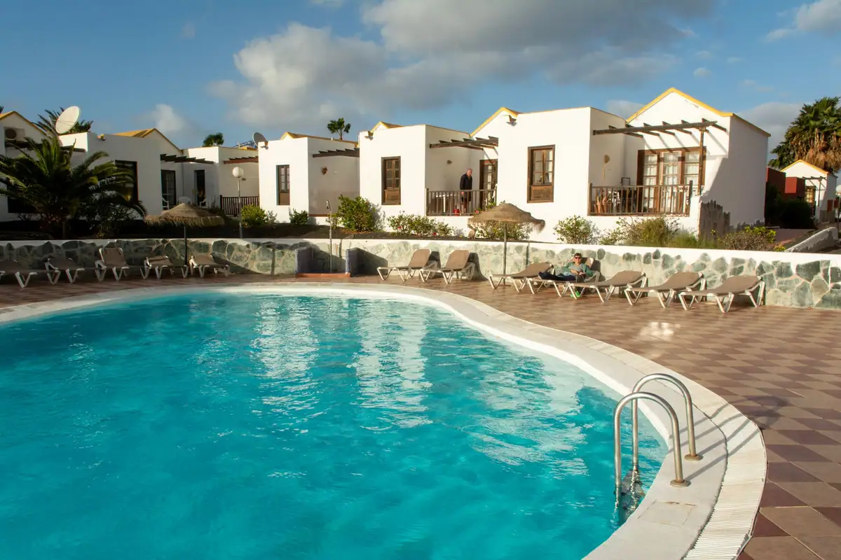 Complejo de bungalós blancos de una planta con piscina comunitaria y tumbonas