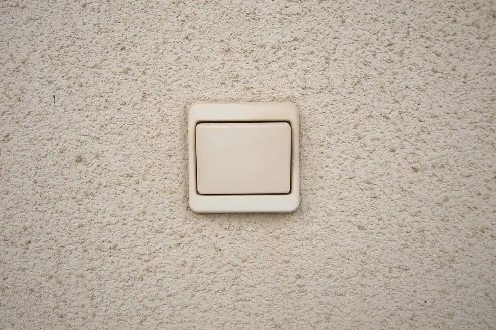 Interruptor antiguo de color crema en una pared rugosa, propio de una instalación eléctrica de otra época