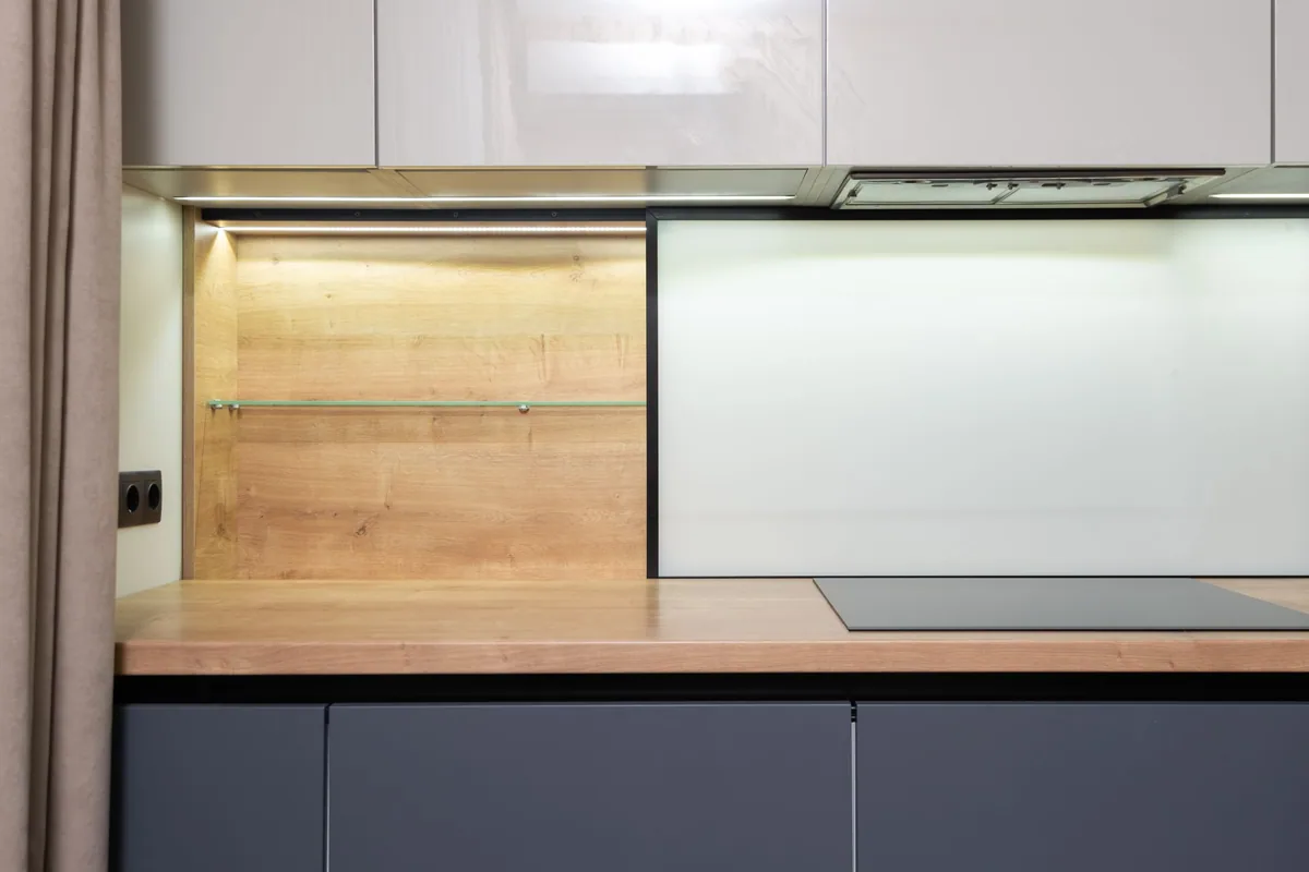 Cocina reciente con placa eléctrica empotrada en la encimera de madera y un enchufe doble en la pared