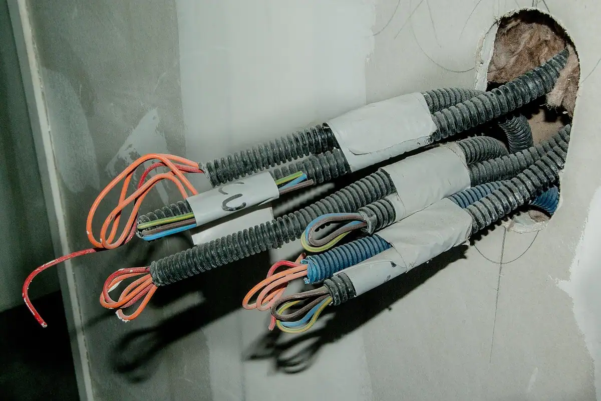 Tubos corrugados con cables nuevos saliendo de un hueco en la pared durante una reforma eléctrica de vivienda